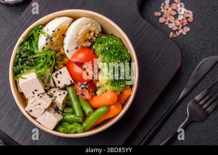 Veganer Salat, Schüsseln mit Kichererbsen, Brokkoli, Tomaten, Tofu-Käse und gekochten Eiern. Vegetarische Mahlzeit mit Gemüse, Samen und Körnern Stockfoto