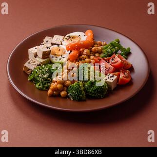 Veganer Salat, Schüsseln mit Kichererbsen, Brokkoli, Tomaten, Tofu-Käse und gekochten Eiern. Vegetarische Mahlzeit mit Gemüse, Samen und Körnern Stockfoto