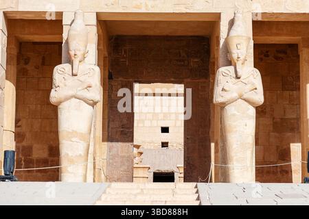 Der Eingang zum Leichentempel der Hatschepsut, der dem Sonnengott Amun-Ra gewidmet ist, in Luxor, Ägypten, wird von zwei Statuen flankiert Stockfoto