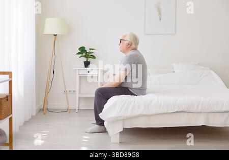 Der Großvater ist unglücklich allein zu Hause, der ältere Mann sitzt auf dem Bett, der schlaflose, reife Patient leidet Stockfoto