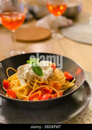 Teller Spaghetti mit Stracciatella-Käse, Kirschtomaten und Basilikum, bereit zum Genießen mit zwei Gläsern aperol Spritz im Hintergrund, in P Stockfoto