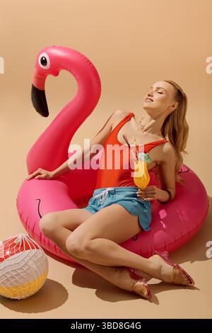 Am Pool entspannt sich eine schöne Frau bei einem erfrischenden Getränk auf einem skurrilen Flamingowagen. Stockfoto