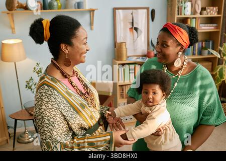 Zwei afroamerikanische Frauen unterhalten sich gern, während sie ihr Kind während eines Familientreffens zu Hause in der Hand halten Stockfoto
