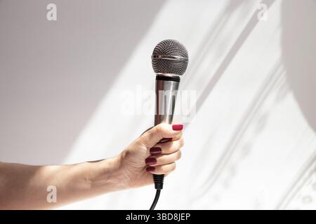Weibliche Hand mit grauem Mikrofon auf hellem Hintergrund mit Schatten, Nahaufnahme Stockfoto