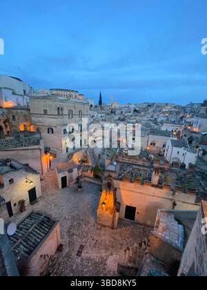 Warme Beleuchtung, die goldenes Licht über verwitterten Steinhäusern von Matera wirft und historischen Charme während der Dämmerung offenbart Stockfoto