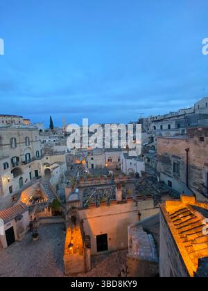 Warme Beleuchtung, die während der Dämmerung goldenes Licht über die alten Steinhäuser von Sassi di Matera wirft und die historische Landschaft der Basilicata unter sanften Bedingungen enthüllt Stockfoto