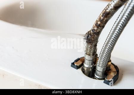 Die Anschlussschläuche des Wasserhahns, von denen einer geplatzt ist und Wasser unter Druck austritt Stockfoto