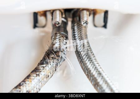 Die Anschlussschläuche des Wasserhahns, von denen einer geplatzt ist und Wasser unter Druck austritt Stockfoto