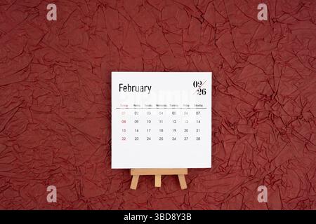Kalender vom Februar 2026 auf rotem, zerknittertem Papierhintergrund. Direkt darüber. Flache Lagen. Stockfoto