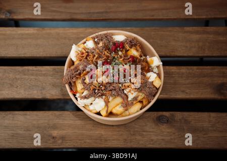 Poutine-Pommes mit Käse und Schweinefleisch in einem Papierbehälter zum Mitnehmen. Köstliche frisch zubereitete Mahlzeit, perfekt für Menüs, Restaurants oder Essenslieferungen Stockfoto