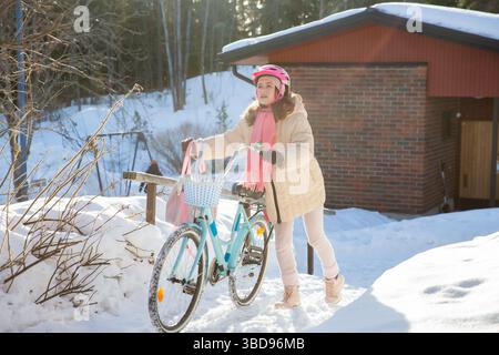Tween geht mit ihrem Fahrrad nach Hause an einem sonnigen Wintertag in einem finnischen Vorort. Schnee auf dem Boden, ein echter Moment des nordischen Alltags. Stockfoto
