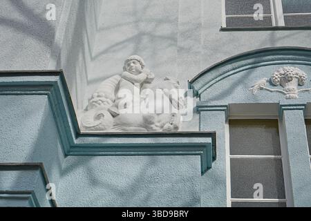 Stuckskulptur und zentrales Motiv an einer historischen Berliner Fassade mit Schatten von fallenden Bäumen und strukturierter blauer Wand bei Tageslicht Stockfoto