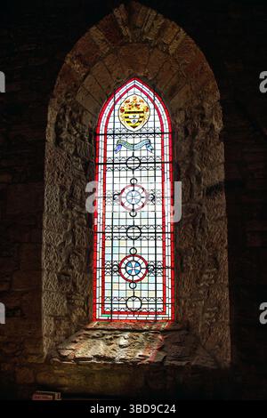 Wunderschönes Buntglasfenster in einer alten Steinmauer mit komplexen geometrischen Mustern und farbenfrohen Designs. Stockfoto