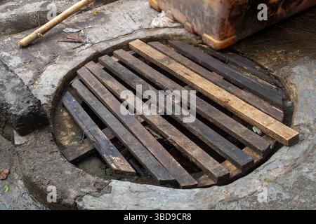 Das Gitter besteht aus Holz und befindet sich in einem Loch im Boden. Das Gitter ist schmutzig und hat eine braune und schwarze Farbe Stockfoto