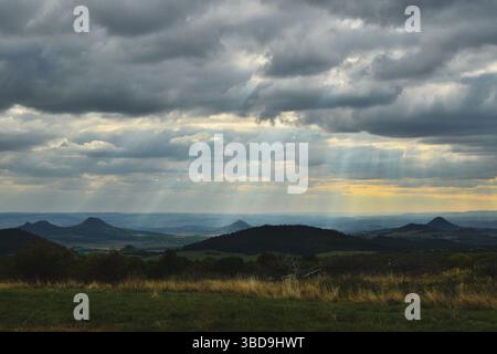 Sonnenlicht bricht am frühen Morgen durch den bewölkten Himmel über ruhigen Feldern und Hügeln Stockfoto