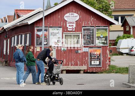 Familie vorbei an einem alten Gebäude mit Ankündigungen und Plakaten im Hafen von Grebbestad an der Westküste Schwedens, Mai 2025 Stockfoto