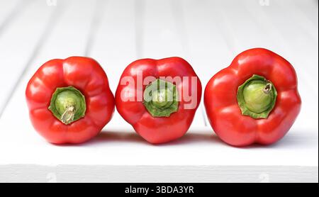 Drei rote Paprika. Frisches Gemüse auf weißem Holz. Gesunde Bio-Lebensmittel Nahaufnahme. Minimale Küchenzusammensetzung. Helle Farbe und Textur. Stockfoto