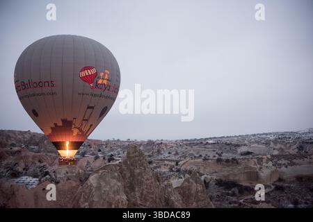 Ein Heißluftballon steigt langsam auf, wenn die Dämmerung über Kappadokien bricht und beleuchtet die einzigartigen Felsformationen und das weiche Gelände darunter. Stockfoto
