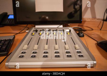 Eine Audio-Mischkonsole ist in einem Tonstudio mit mehreren Schiebereglern und Tasten, die von sanften Lichtern beleuchtet werden, übersichtlich angeordnet. Stockfoto