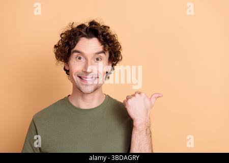 Glücklicher junger Mann mit lockigen Haaren, der ein khakifarbenes T-Shirt trägt, das auf einen beigefarbenen Hintergrund zeigt Stockfoto