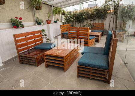 Eine gemütliche Terrasse im Lounge-Stil mit Holzstühlen, gepolsterten Sitzen und kleinen runden Tischen unter einem Baldachin, die eine entspannte Ecke für Gespräche und Gespräche schaffen Stockfoto