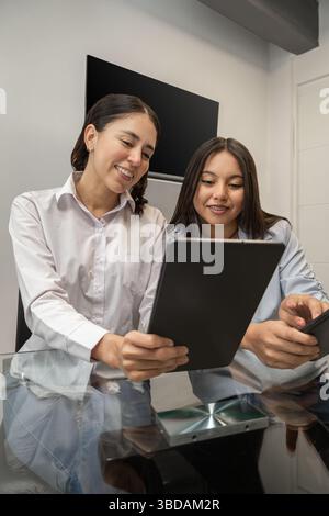Zwei junge Frauen teilen einen freudigen Moment, während sie gemeinsam ein Tablet betrachten, das Freundschaft, Technologie und positive Verbindungen in einem modernen setti widerspiegelt Stockfoto