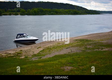 Eine kleine Motoryacht hat am Ufer des Flusses angedockt. Motorboot an der Flussseite vor Anker. Stockfoto