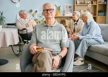Porträt eines älteren Mannes, der mit Buch im modernen Wohnzimmer sitzt Stockfoto