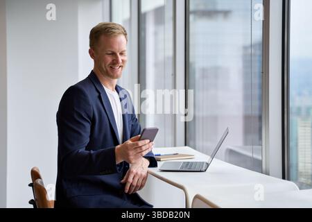 Glücklicher Geschäftsmann, Investor, der im Büro ein Smartphone weckt. Stockfoto
