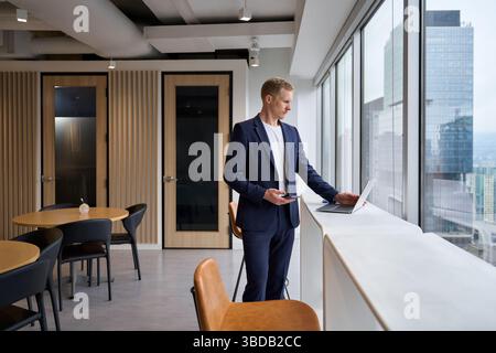 Beschäftigter junger Geschäftsmann im Büro, der am Laptop mit dem Telefon arbeitet. Stockfoto