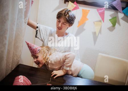 Geschwister genießen einen spielerischen Moment während einer Geburtstagsfeier zu Hause Stockfoto