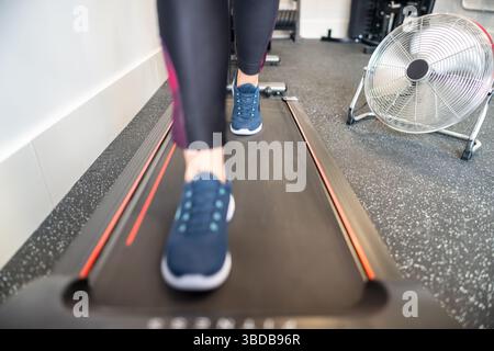 Frauenbeine gehen auf einem Laufband in einem Fitnessstudio mit einem Ventilator. Stockfoto