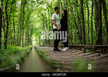 Ein romantisches Paar genießt einen gemeinsamen Moment auf einer malerischen Eisenbahn im Wald Stockfoto