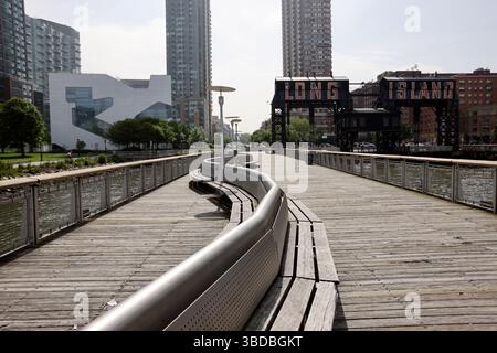 Breiter Spaziergang in der Morgensonne um den Gantry Plaza State Park in Long Island City. Die Sitzplätze am Pier mit Long Island Schild im Hintergrund. Stockfoto