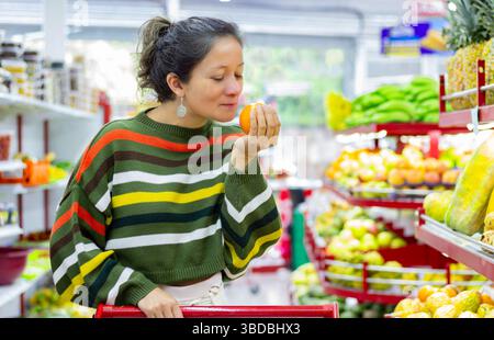 Frau, die eine frische Orange im Supermarkt riecht und die Fruchtqualität bewertet. Gesunder Lebensstil, achtsames Einkaufen, Naturkost, Lebensmittelgeschäft Stockfoto