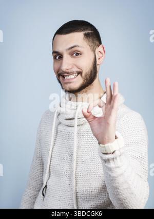 Der junge gutaussehende Mann zeigt das OK-Zeichen auf blauem Hintergrund Stockfoto
