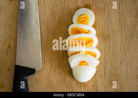 Geschnittenes gekochtes Ei auf einem hölzernen Schneidebrett mit Küchenmesser, Blick von oben. Stockfoto
