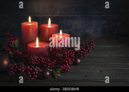 Dunkelrote Adventsdekoration mit für beleuchtete Kerzen, Berrie-Dekoration und Weihnachtskugeln vor rustikalem Holzhintergrund, Kopierraum, ausgewählter Fokus Stockfoto