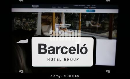 In dieser Fotoabbildung hält eine Person ein Handy mit dem Logo des spanischen Gastgewerbeunternehmens Grupo Barcelo auf dem Bildschirm vor der Webseite. Stockfoto