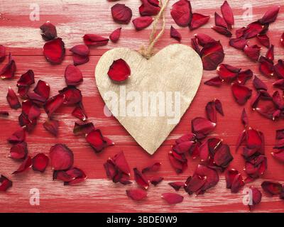 Rustikales Holzherz mit Rosenblättern auf roten Holzbohlen Stockfoto