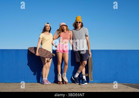 Gruppe junger Skater posiert mit Skateboards und Rollschuhen an einer blauen Wand Stockfoto
