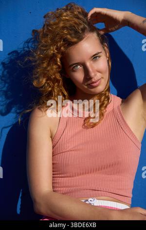Eine junge Frau mit lockigen roten Haaren, die sich an der blauen Wand posiert Stockfoto