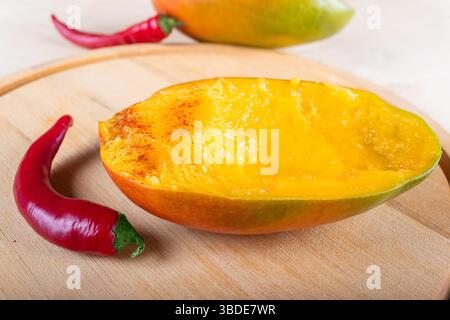 Seitenansicht von zwei Hälften Mango und zwei roten heißen Chilischoten auf hölzernem Hintergrund, Nahaufnahme Stockfoto