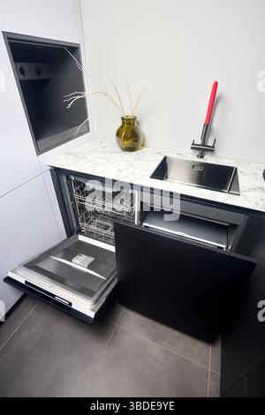Küche mit eingebautem, geöffnetem Geschirrspüler und herausziehbarer Schublade für die getrennte Abfallsammlung. Wasserhahn Waschbecken mit kompaktem Hochdruck Stockfoto