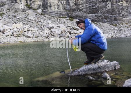 Bergsteiger auf einem Felsen in einem See, der während einer Kletterexpedition Trinkwasser in den Anden von Peru pumpt und filtert Stockfoto