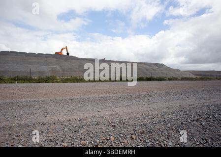 Blick auf eine neue Straße im Bau mit einem Frontlader bei der Arbeit in großer Entfernung auf einem Hügel aus Material Stockfoto
