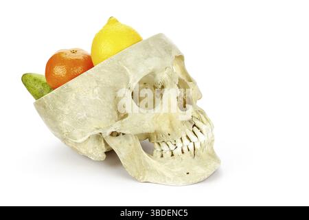 Menschlicher Schädel als Obstwaage mit Früchten wie Zitronen Orangen und Birnen isoliert auf weißem Hintergrund Stockfoto