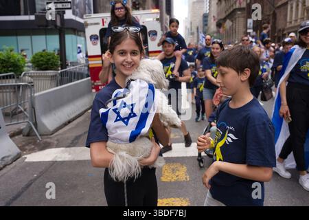 Ein Mädchen hält einen kleinen weißen Hund, der bei einer Parade in eine israelische Flagge gehüllt ist. Andere Teilnehmer und Zuschauer sind im Hintergrund zu sehen. Die Gesamt- se Stockfoto
