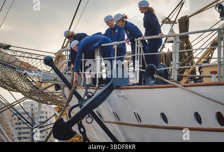 Spanien Malaga 1 28 2024 Seeleute in blauen Uniformen, die auf einem großen Schiff vor Anker in einem belebten städtischen Hafen vor Seefahrt fahren Stockfoto