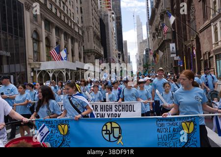 Eine große Gruppe von Teenagern und jungen Erwachsenen, die überwiegend hellblaue T-Shirts tragen, nimmt an einer Parade in einer Stadtstraße Teil. Sie tragen eine große Stockfoto